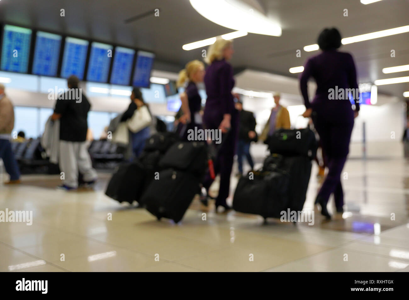 Defocus blurred bokeh of travelers in airport terminal traveling for work and vacation - suitcases, luggage, backpacks, digital flight schedule board Stock Photo