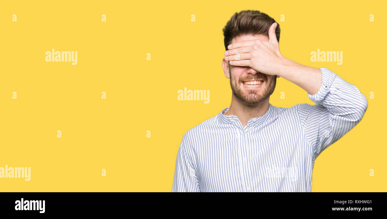 Young handsome man smiling and laughing with hand on face covering eyes ...