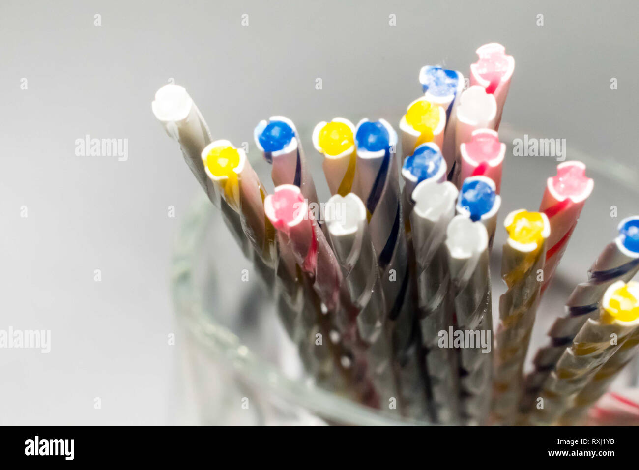 Multi-colored stipes thin candles on a glass mug isolated on a white background Stock Photo