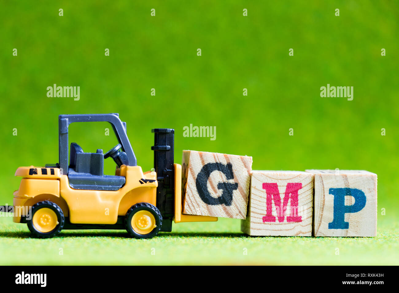 Toy forlift hold letter block G to fulfill word GMP (Abbreviation of Good Manufacturinc Practice) on green background Stock Photo