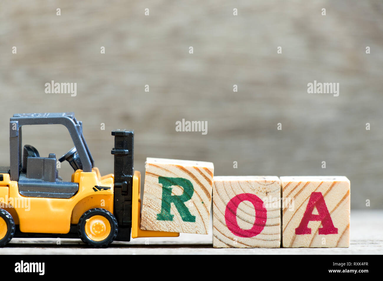 Toy forklift hold letter block  in word ROA (abbreviation of return on assets) on wood background Stock Photo