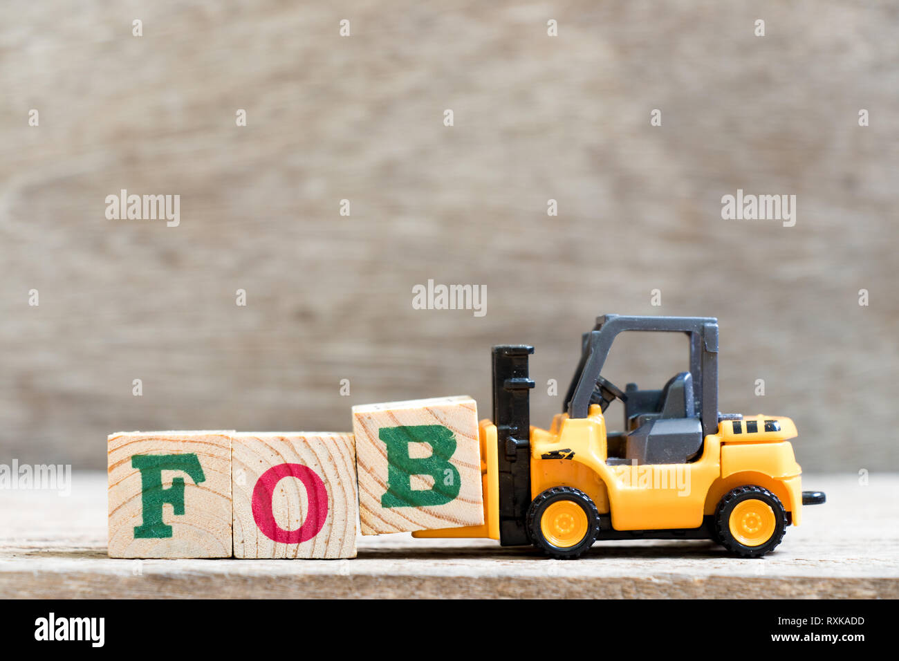 Toy forklift hold letter block B in word FOB (abbreviation of Free On Board) on wood background