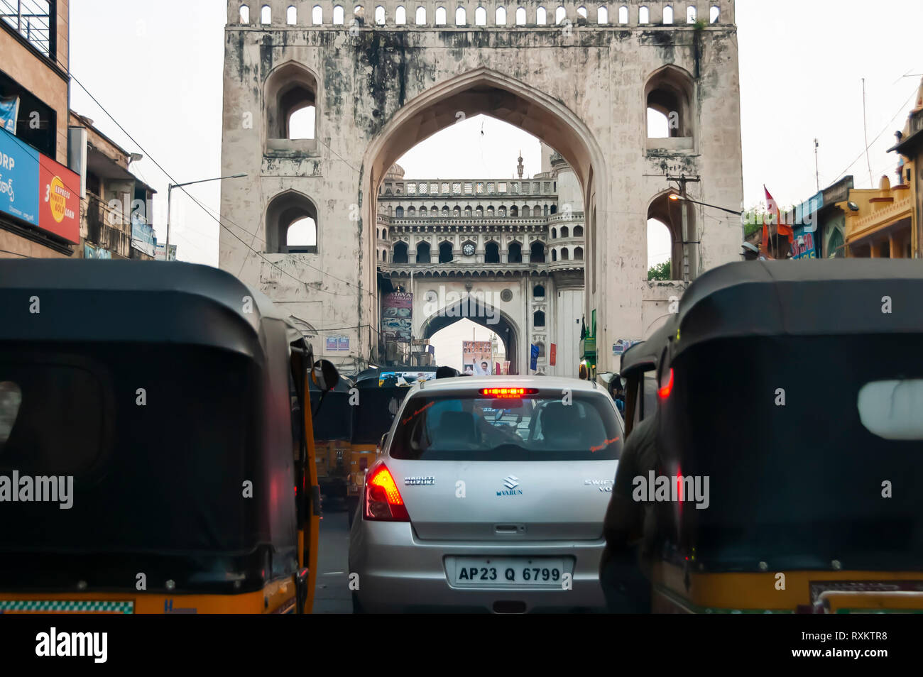 Taken from inside a moving car. Charminar framed by Char Kaman, which in turn is framed by two auto rickshaws (tuk-tuks). Hyderabad, Telangana, India. Stock Photo