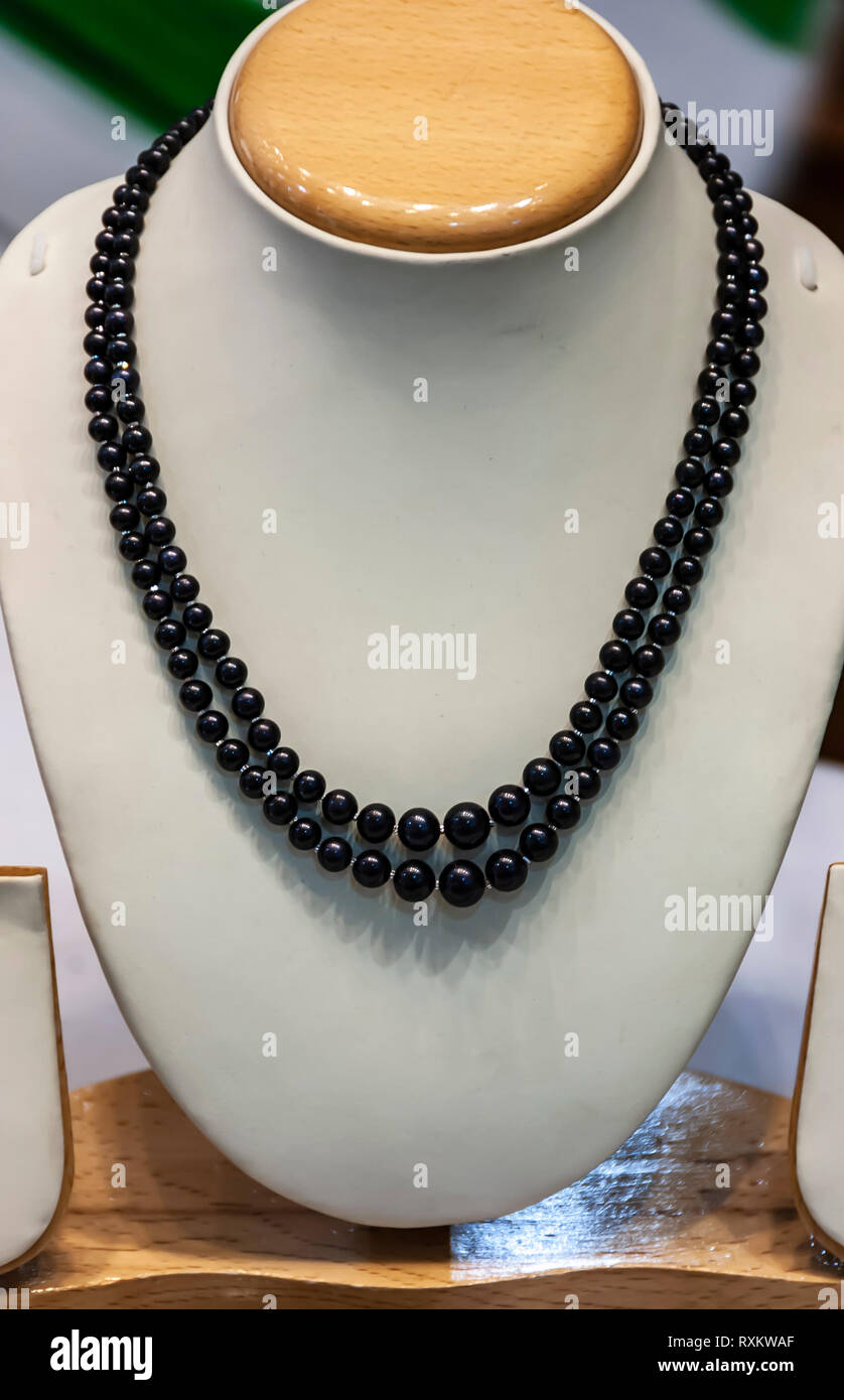 A black pearl necklace hanging on a white neck mold on display