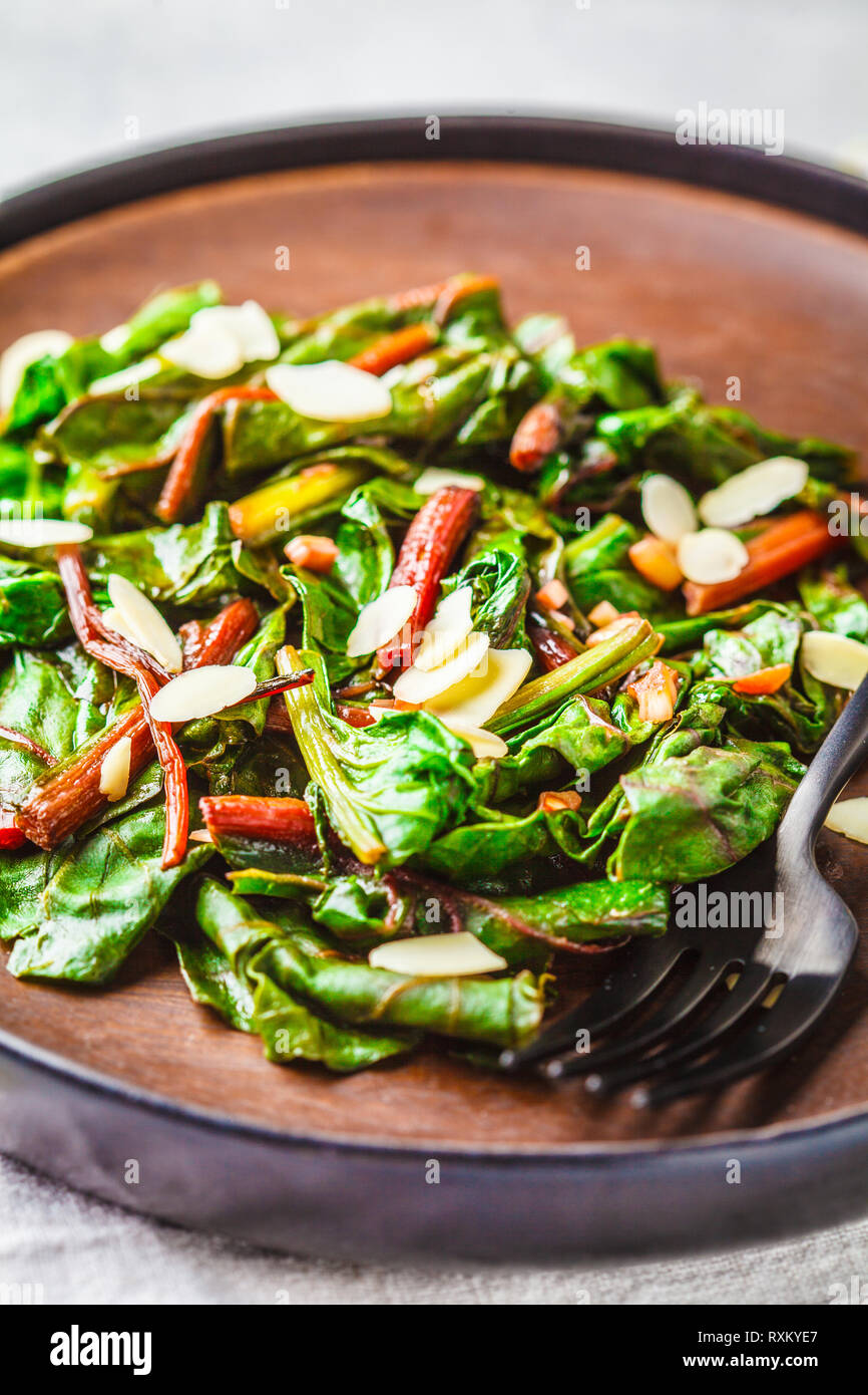 Beet greens salad with nuts in black plate, white background