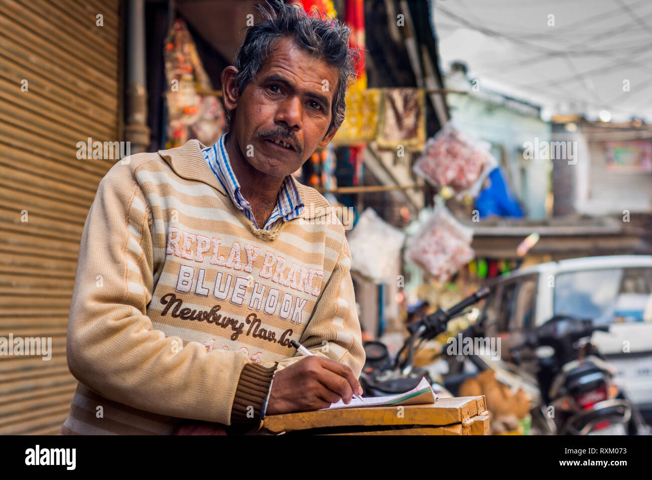 a middle aged Indian man wearing sweater standing, looking at the camera and has a notebook open in the afternoon in winter. He is 50-55 years old. Stock Photo