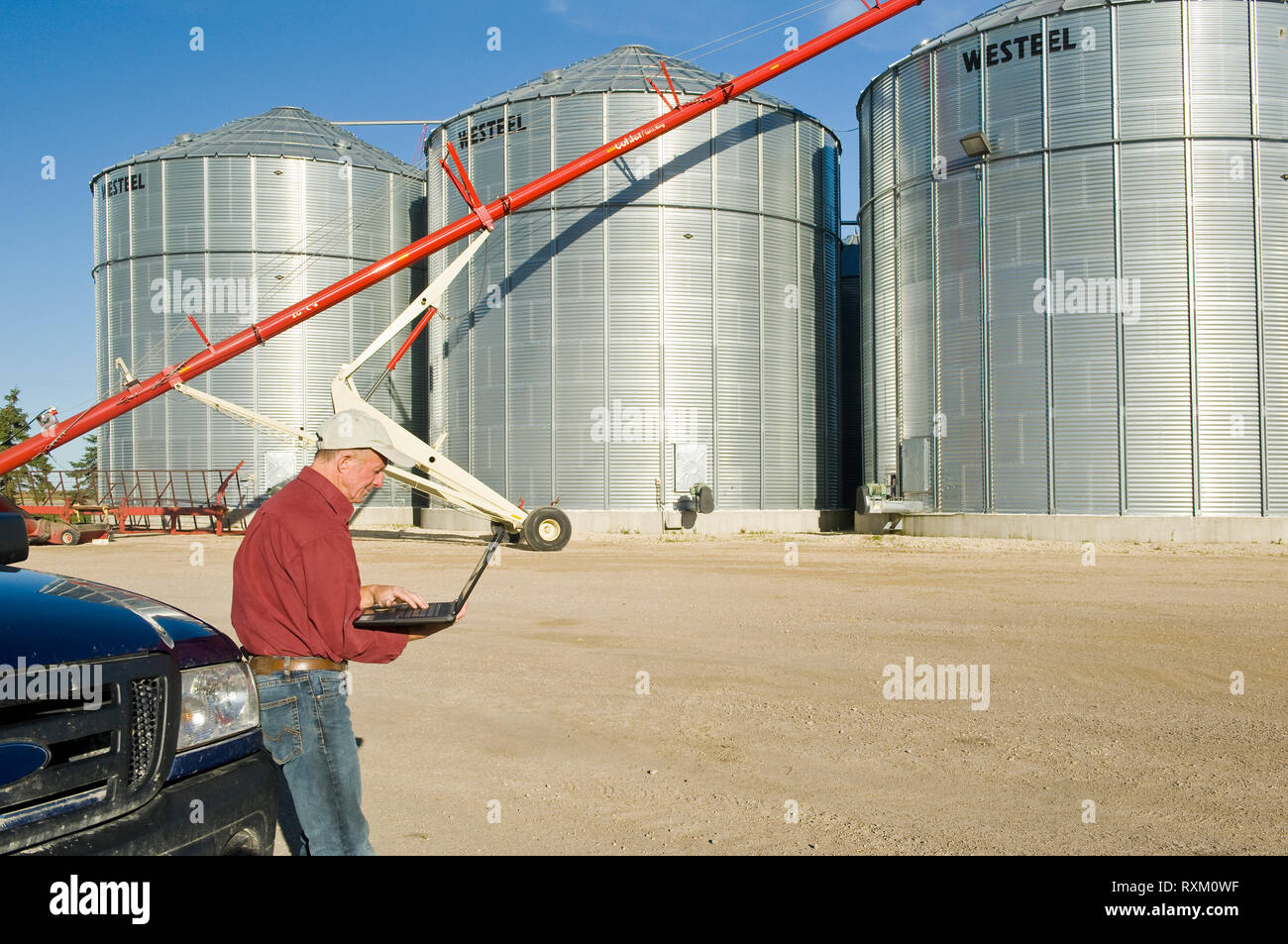 man using a computer next grain bins in a farmyard, near Lorette, Manitoba Stock Photo
