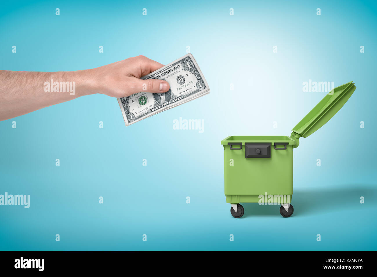 Male hand throwing bundle of money dollars into green trash bin on blue