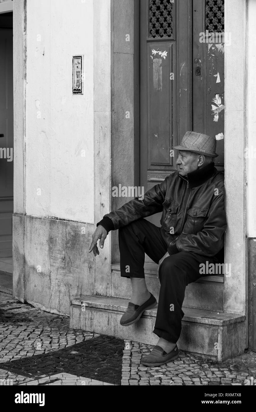 A man sits on a doorstep, corner of Rua Capelão and Rua da Mouraria, Martim Moniz, Lisbon, Portugal.  Black and white version Stock Photo