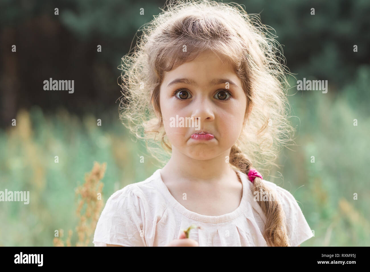 Close up Portrait of beautiful little Girl holding her head in amazement and surprised with something at summer day Stock Photo