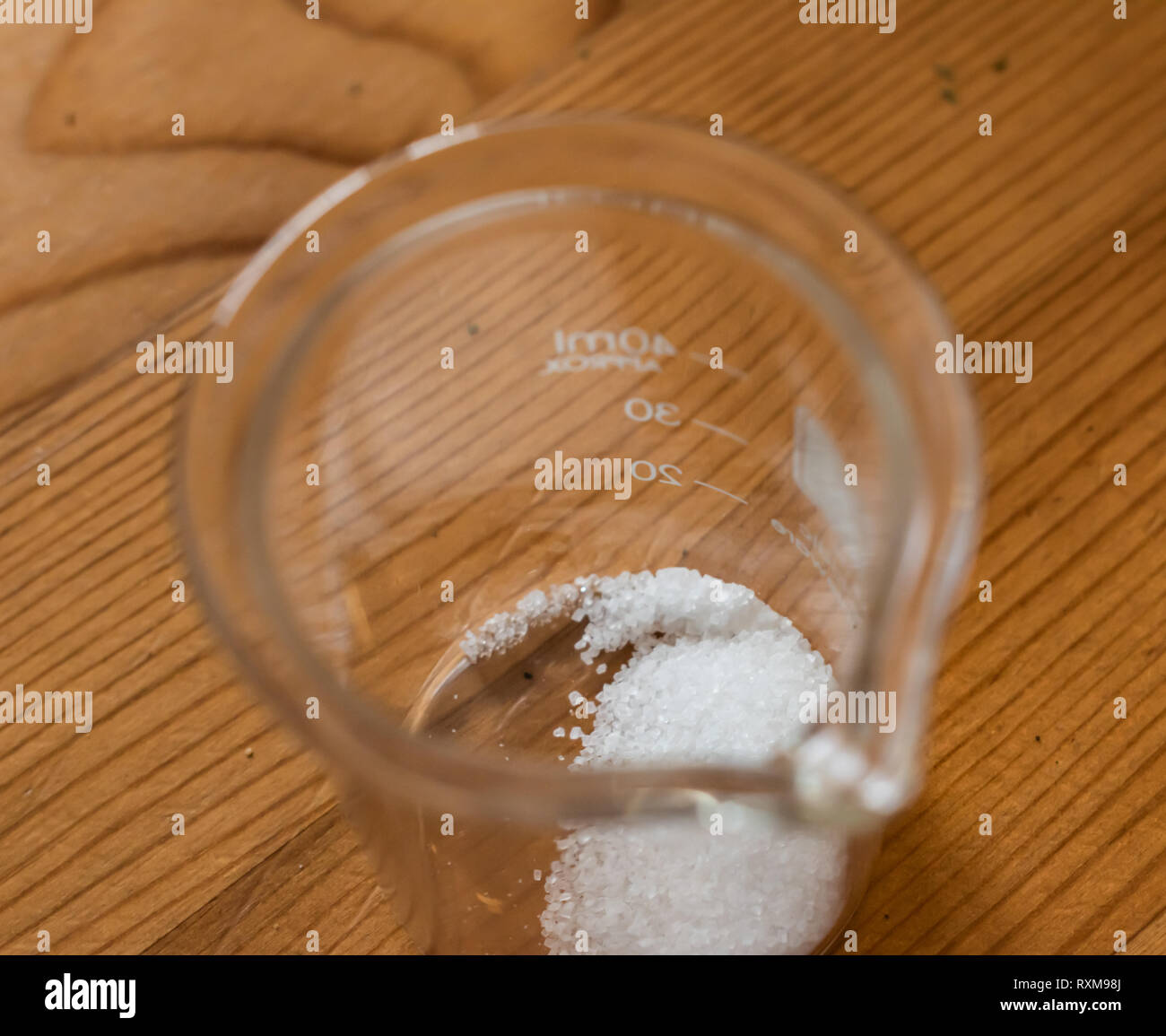 Small 40 mL glass chemistry beaker with small geometric sugar crystals laying in the bottom Stock Photo