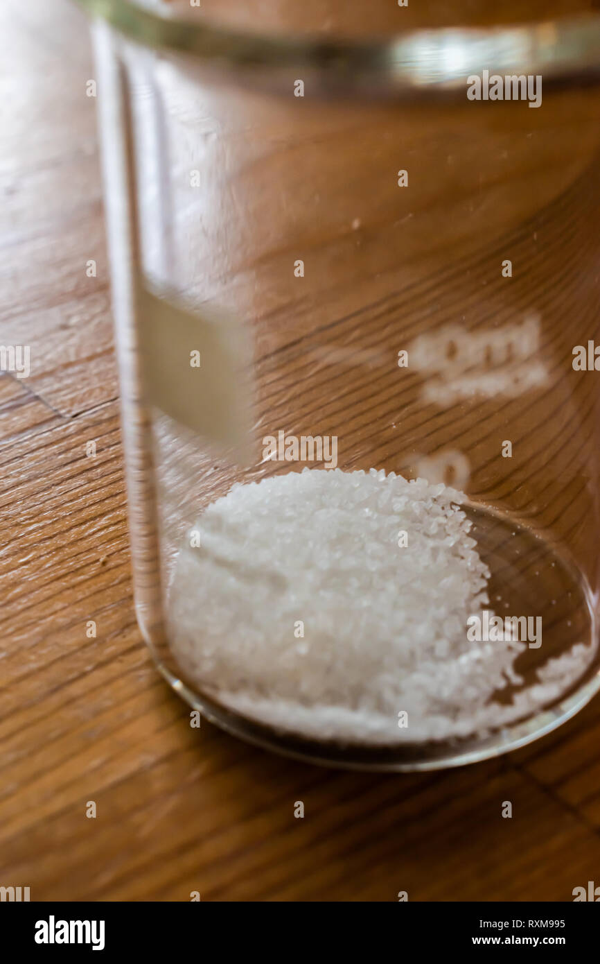 Small 40 mL glass chemistry beaker with small geometric sugar crystals laying in the bottom. Depth of field shot to focus on crystals. Stock Photo