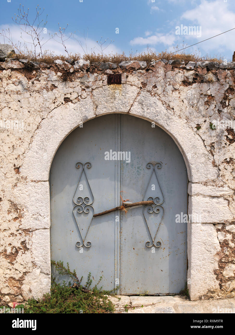 Old curved painted metal door on stone fence under blue sky