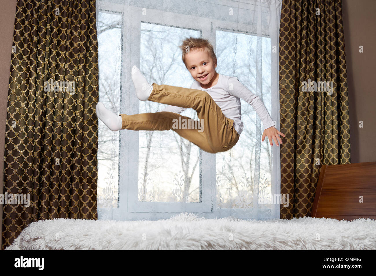 child fun home. Beautiful blond child 6 years old fooling around morning to room. Kid smiling jumping to bedroom on bed. Stock Photo