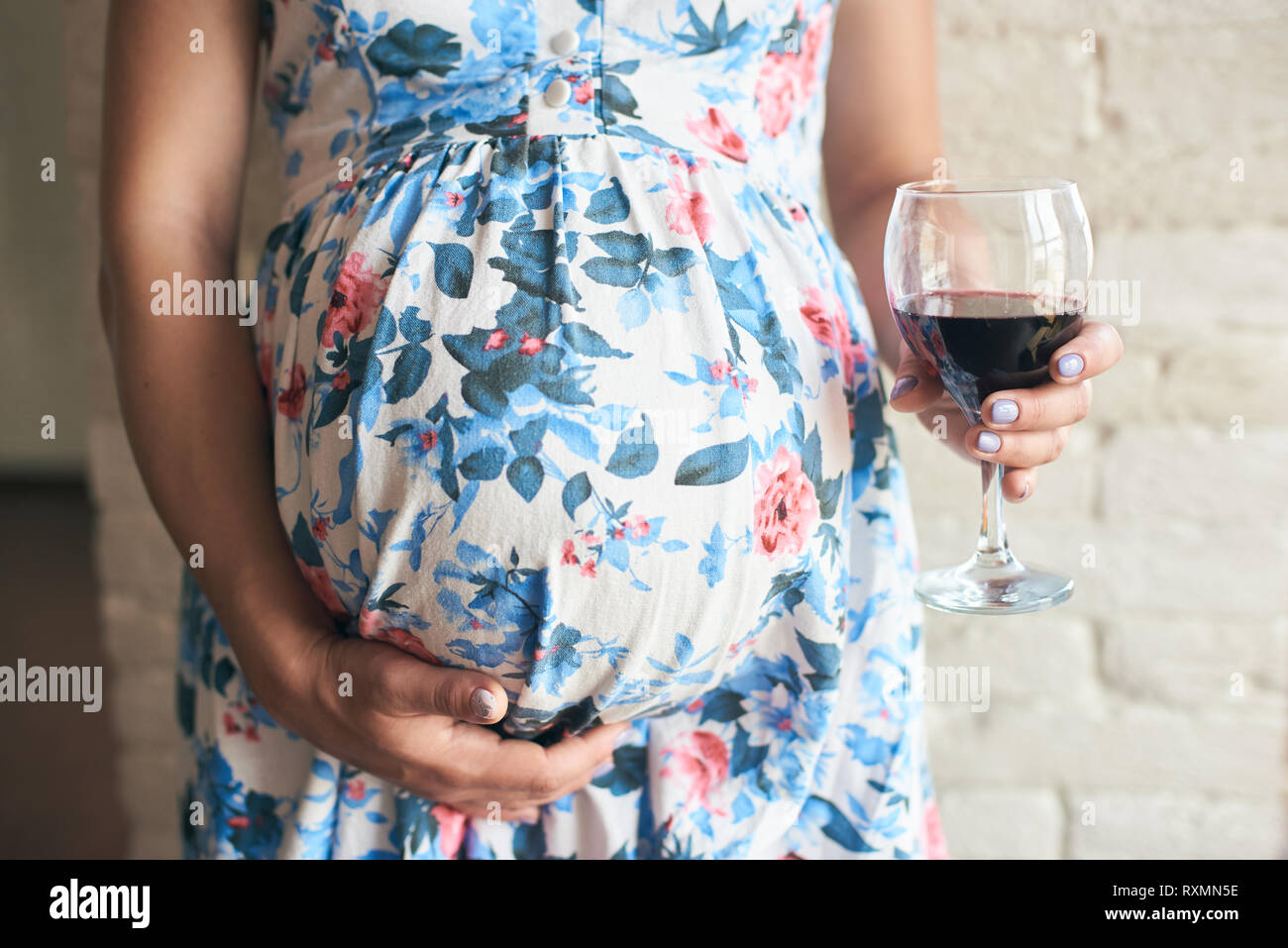 Cropped view, selective focus of glass of wine in hands of pregnant woman. Future mother embracing belly and drinking harmful alcohol while expecting  Stock Photo