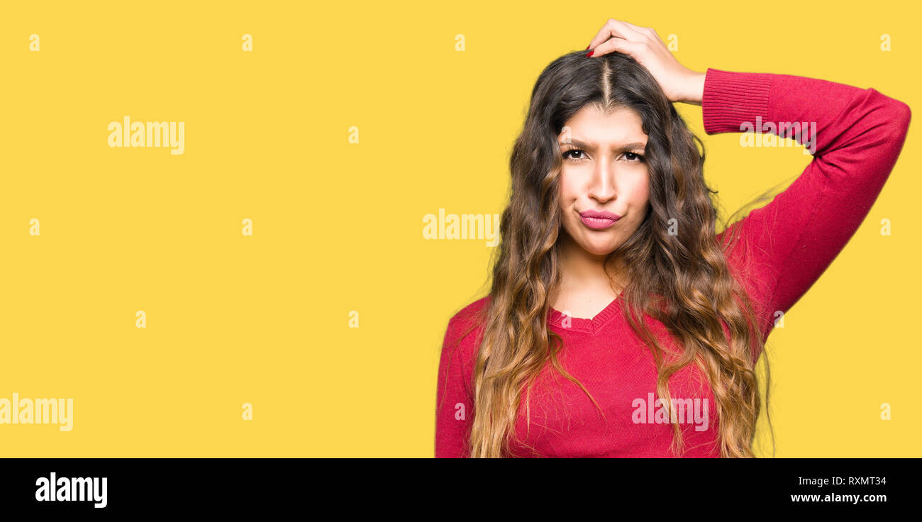 Young beautiful woman wearing red sweater confuse and wonder about question. Uncertain with doubt, thinking with hand on head. Pensive concept. Stock Photo