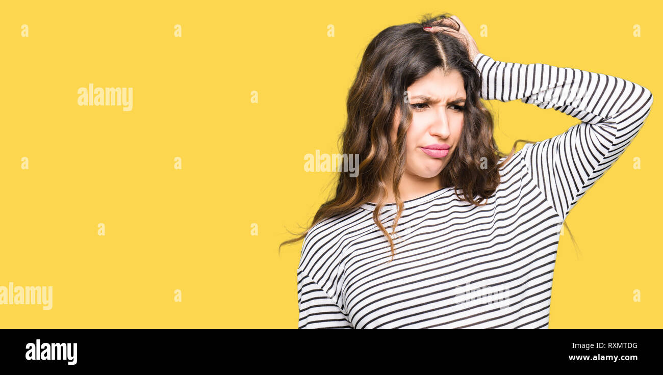 Young beautiful woman wearing stripes sweater confuse and wonder about question. Uncertain with doubt, thinking with hand on head. Pensive concept. Stock Photo