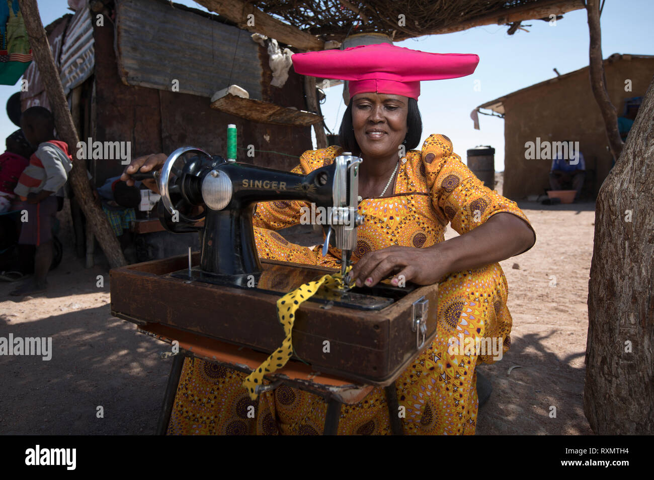 A Herero woman sews miniature dresses for dolls she sells to passing tourists. Stock Photo