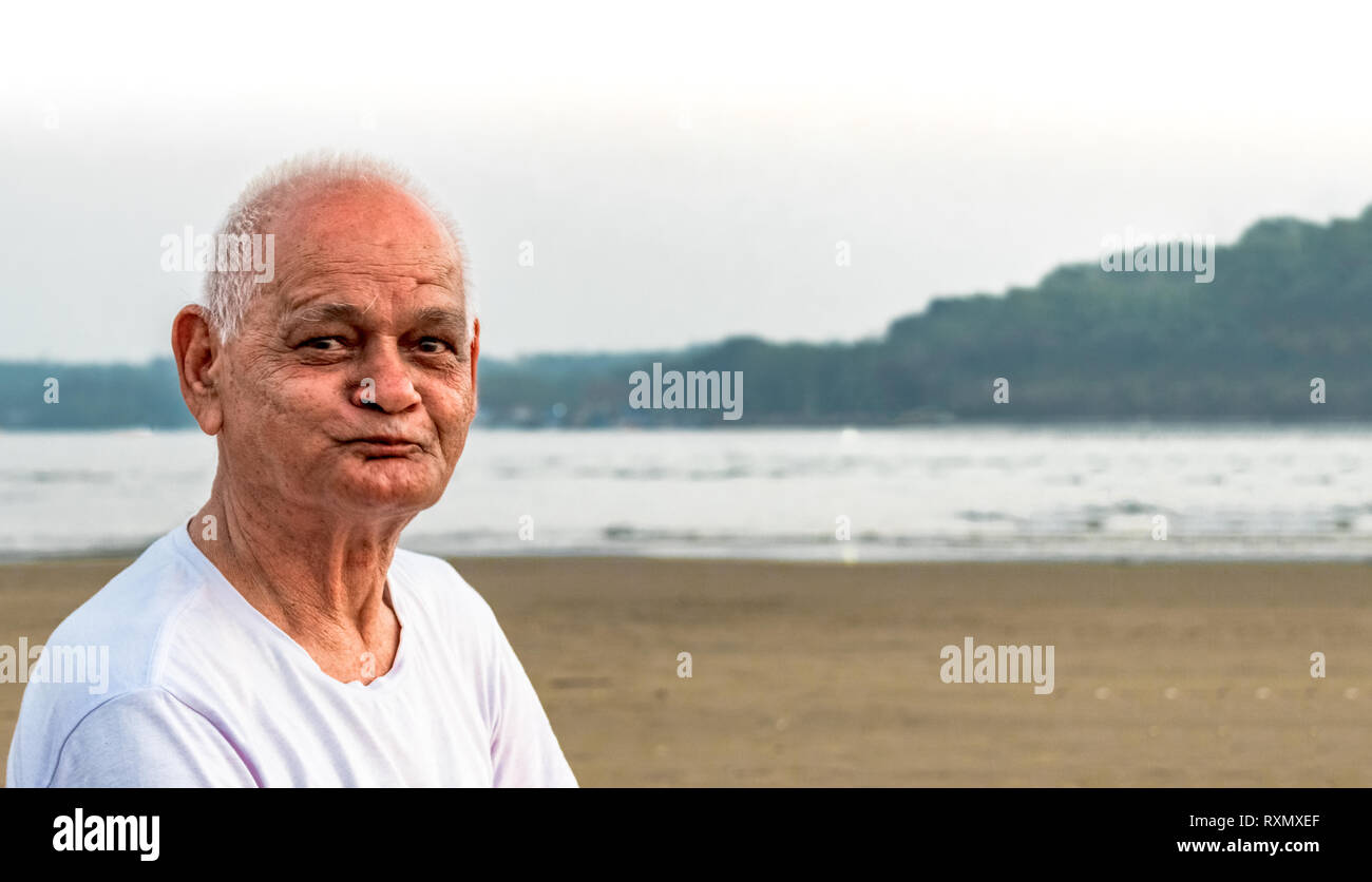 Super Senior Citizen in his mid 80s, posing to camera happily, while making happy faces and enjoying his retired life merrily on a beach Stock Photo