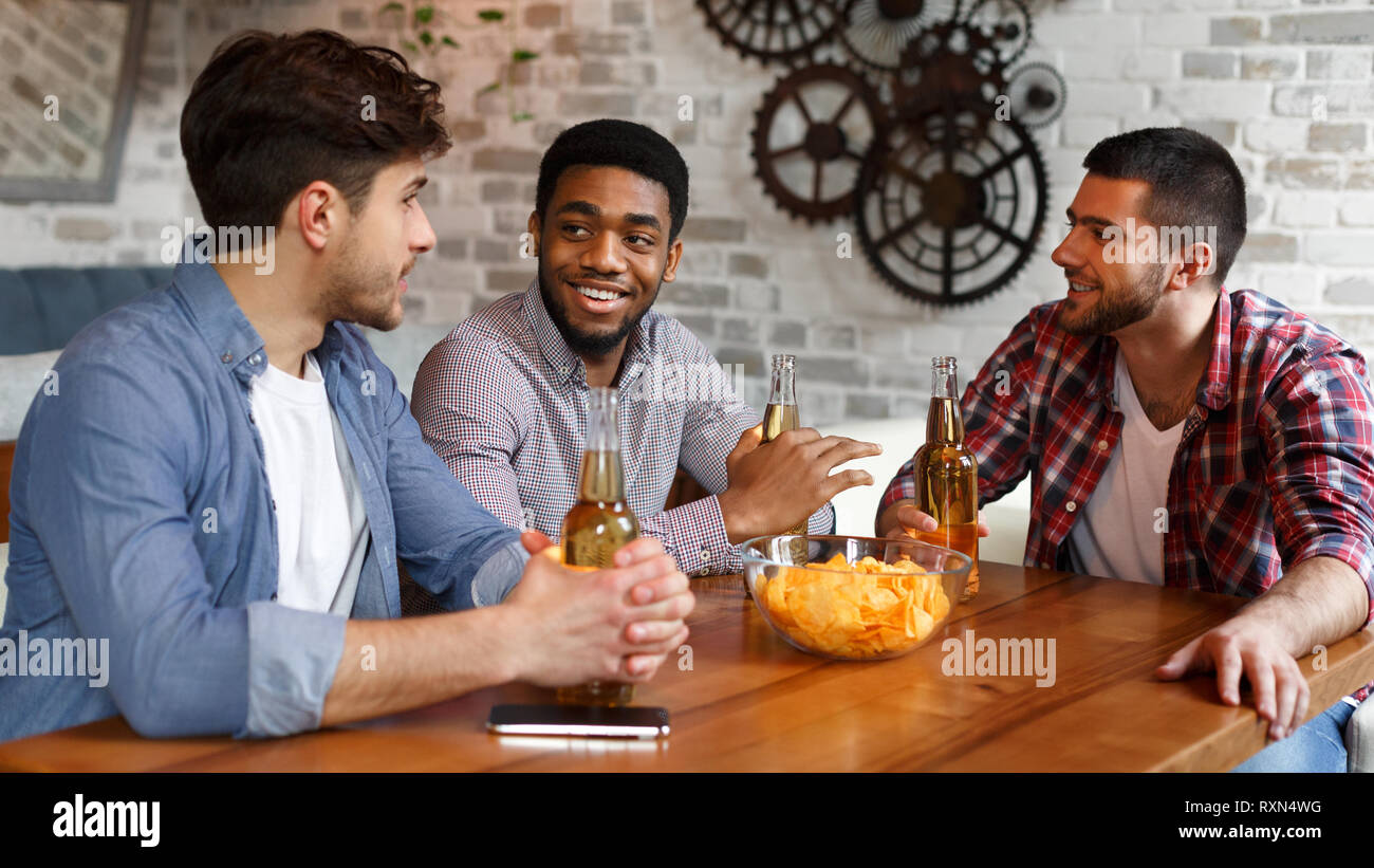 Young men talking, eating chips and drinking beer Stock Photo