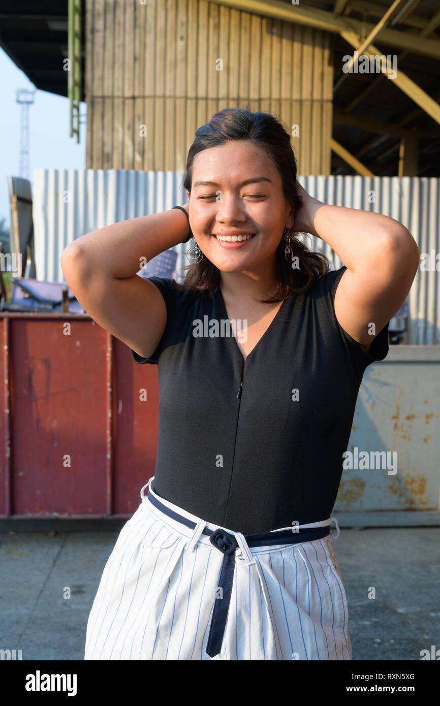 Young happy Asian woman smiling with eyes closed in urban street Stock Photo
