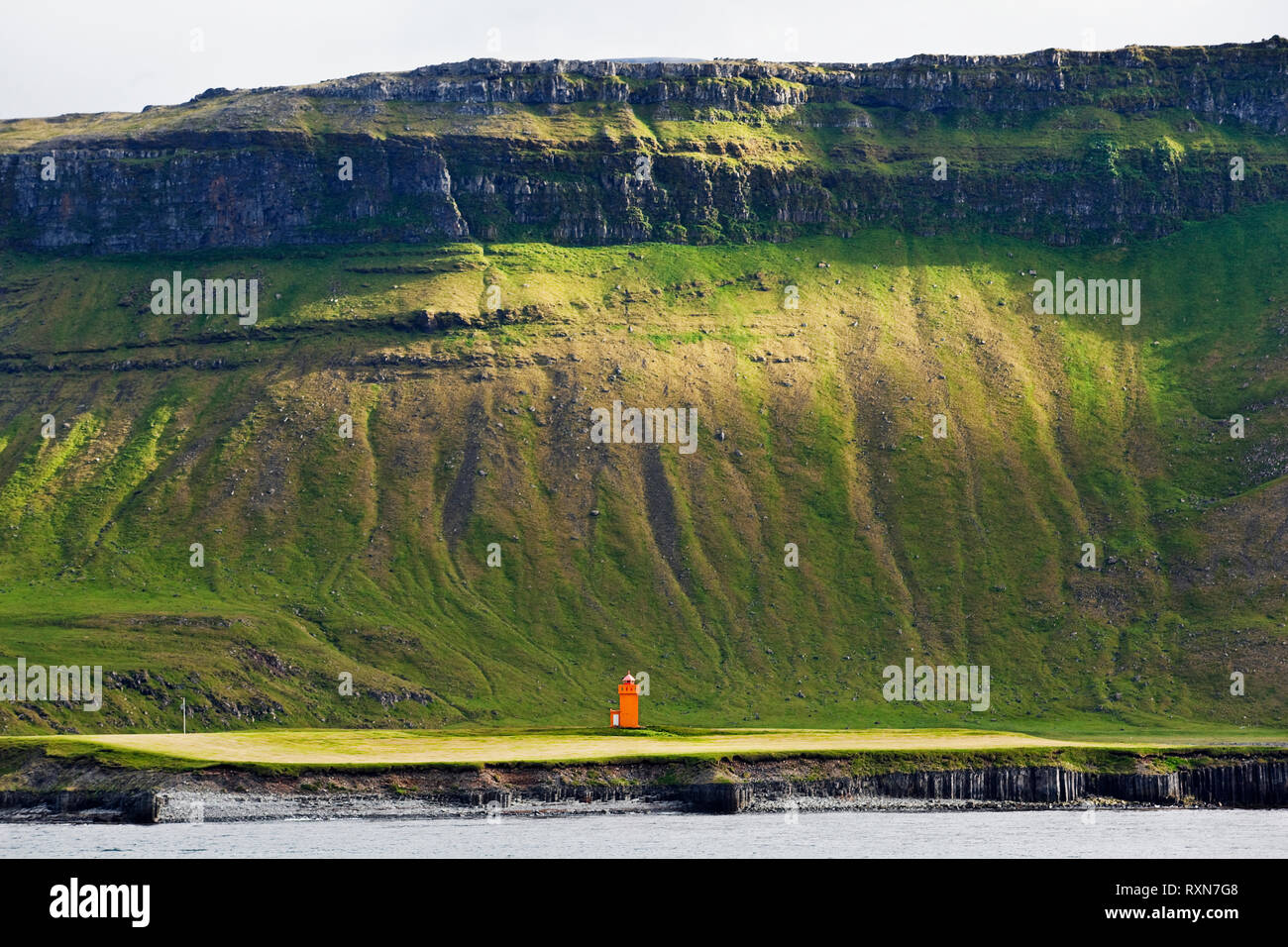 Steep mountainside towering above an orange lighthouse northwest of Grundarfjordur on the Snaefellsnes Peninsula, Iceland Stock Photo