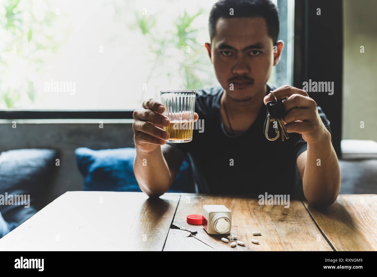 Man holds glass of whiskey and car keys with pills on the table. Stock Photo