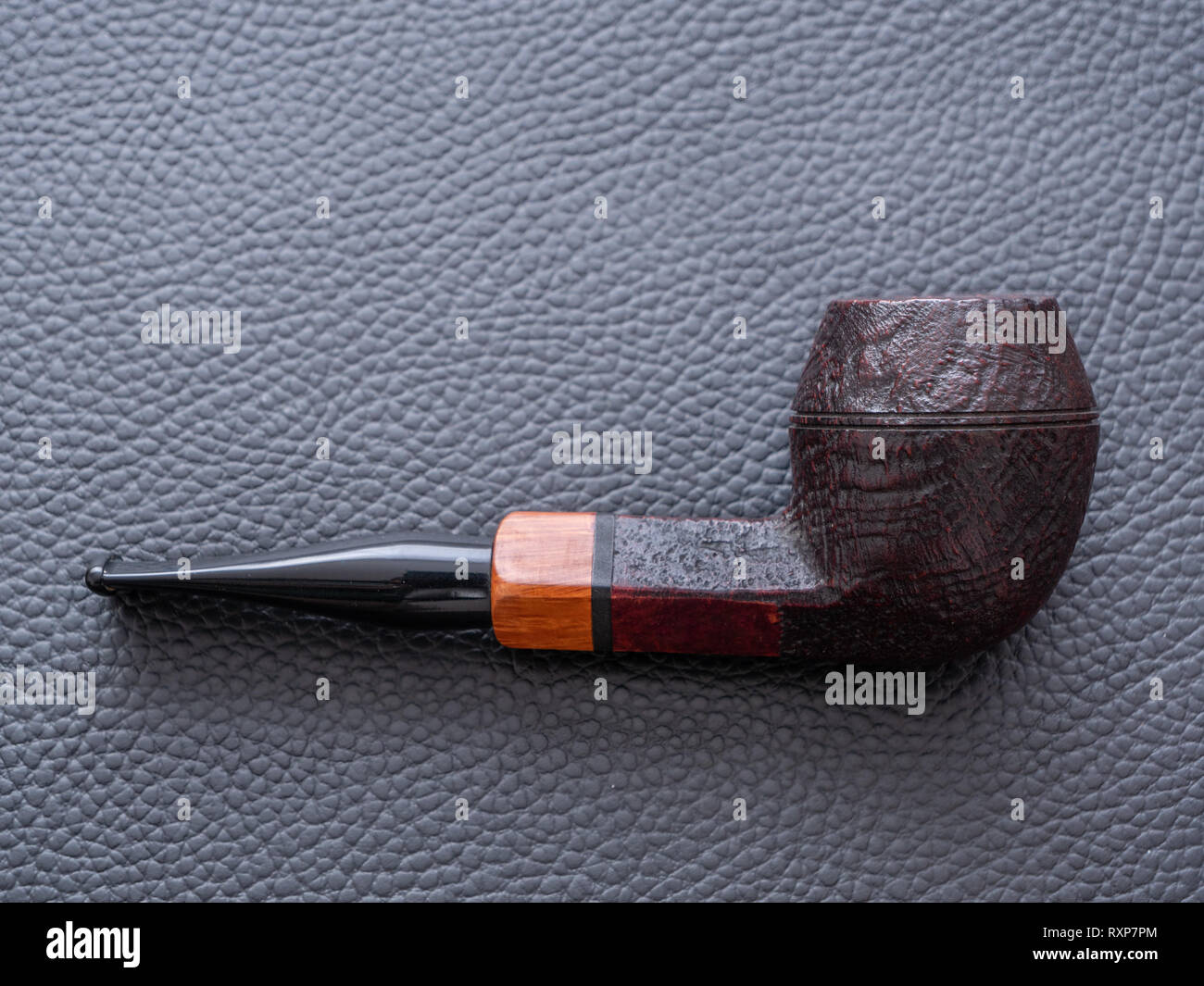 An Old Fashioned Dark Brown Rusticated Army or Bulldog Smoking Pipe on a Black Leather Background - A Concept for Smoking Stock Photo