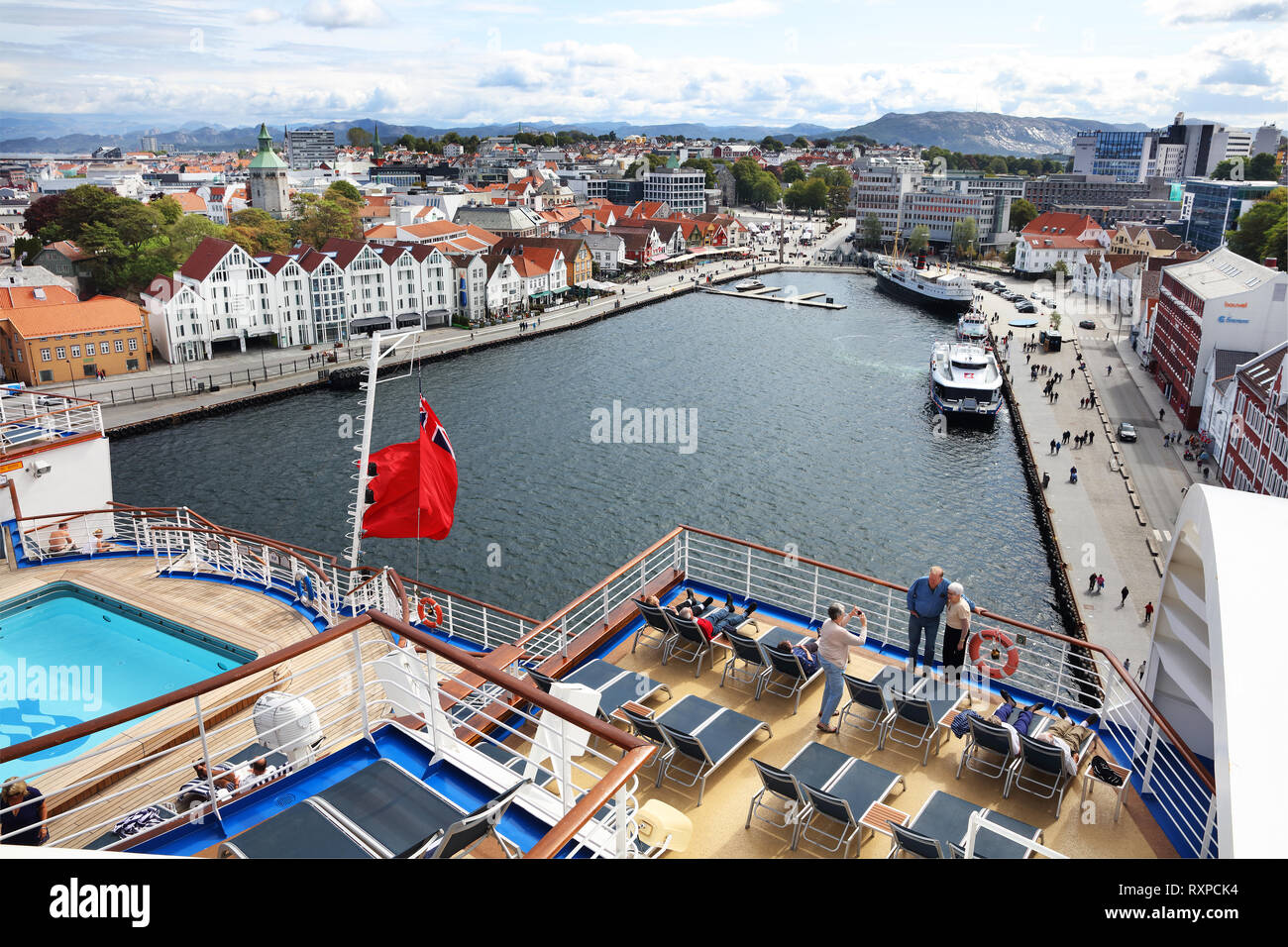 Couple posing for a photo on the upper deck of a cruise ship with Vagen Bay and the city of Stavanger, Norway, in the background. Stock Photo