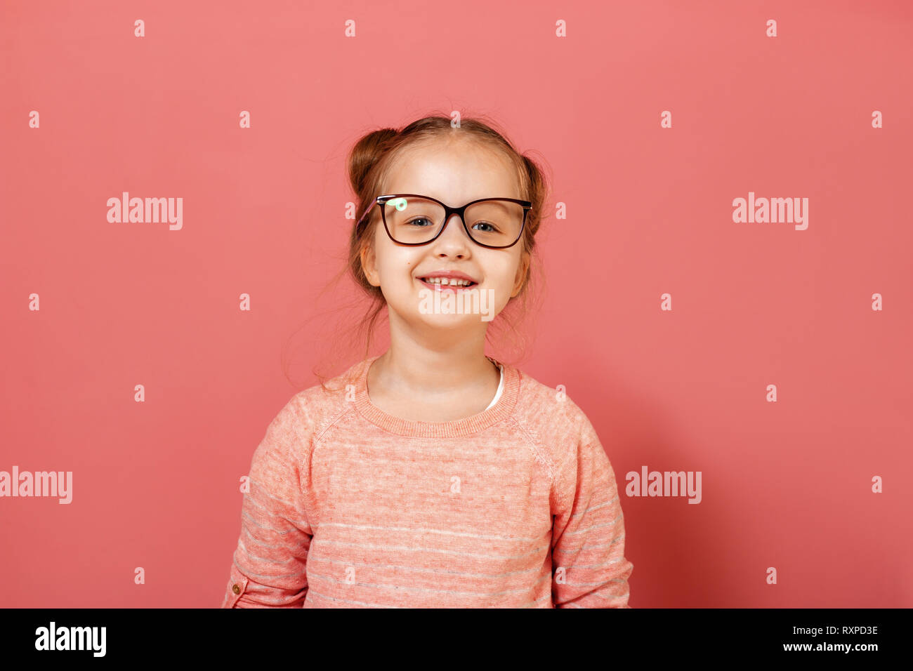 Portrait of a cute little 6 year old girl wearing eyeglasses on a pink background Stock Photo