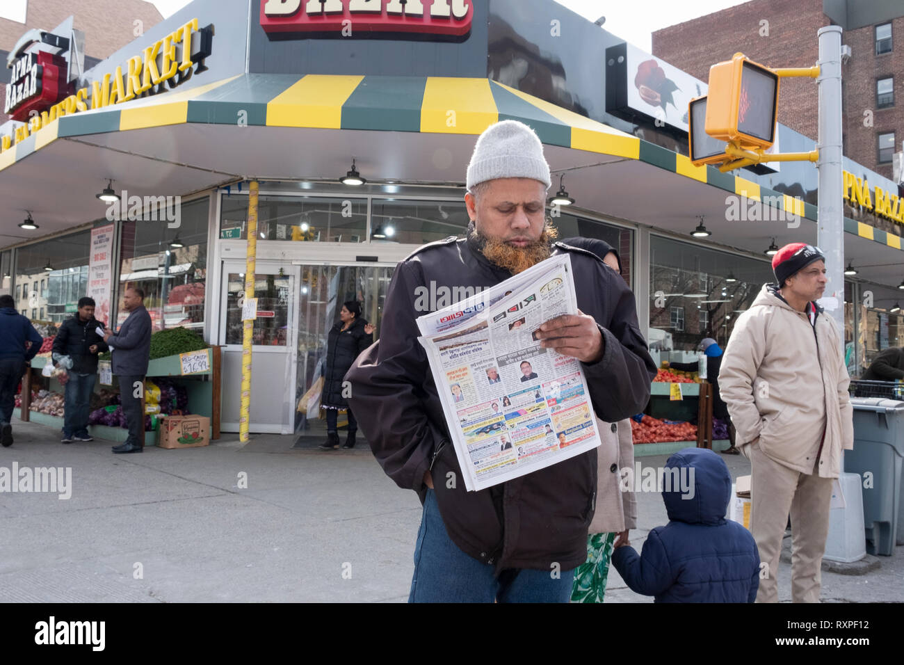 A Muslim man with a henna dyed beard reads a Bengali newspaper on 37th Avenue in Jackson Heights, Queens, New York City. Stock Photo