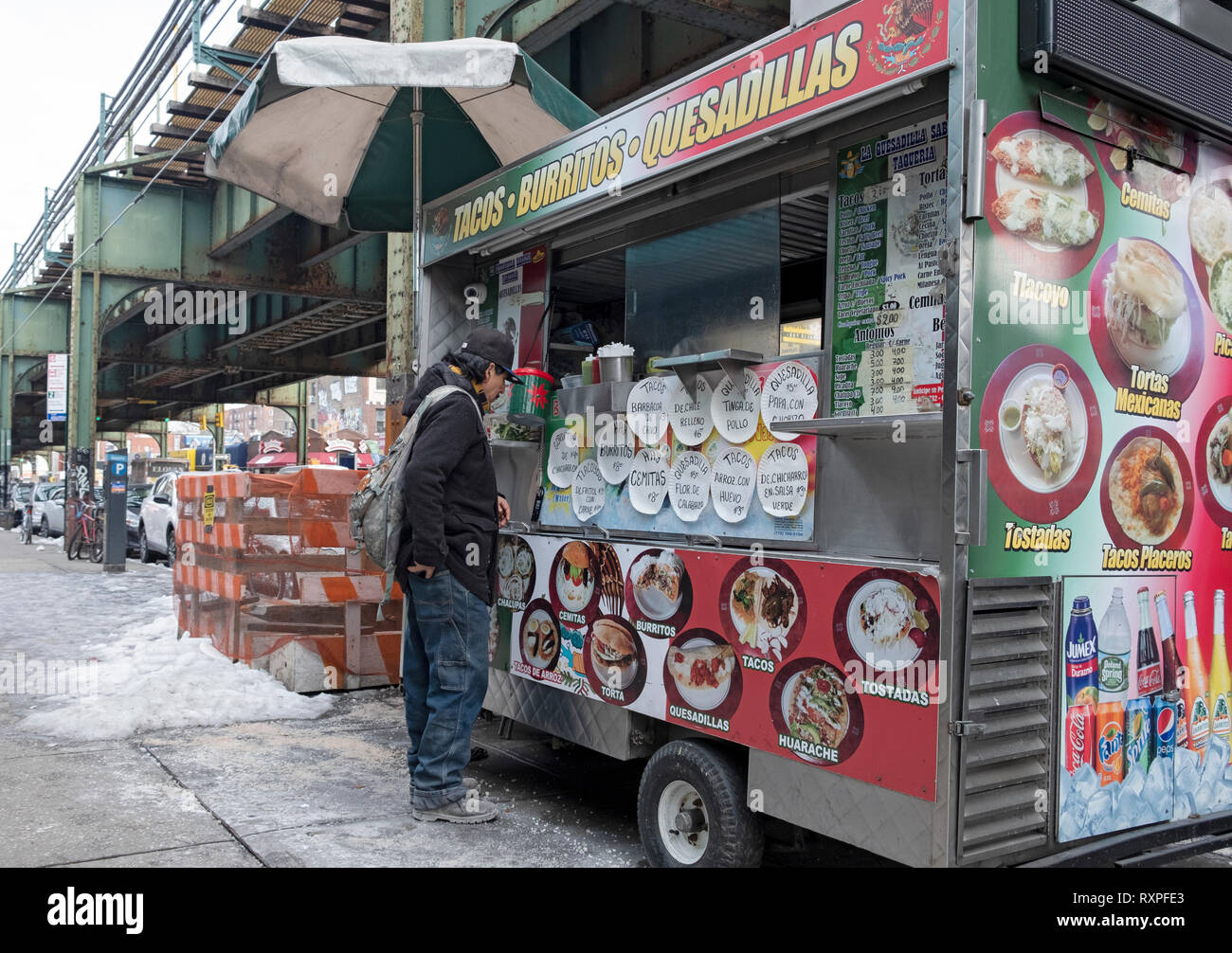 A Latin American worker stops to buy food from a Mexican food cart parked on Roosevelt Ave. under the elevated subway. In Jackson Heights, Queens, NYC Stock Photo