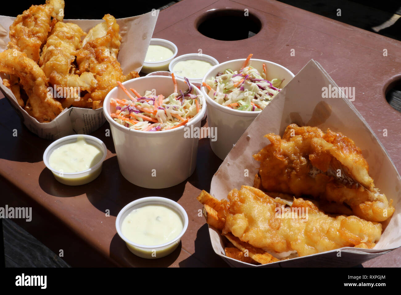 Enjoy tasty fish and chips with coleslaw and tartar sauce at the beach on a sunny day. Stock Photo