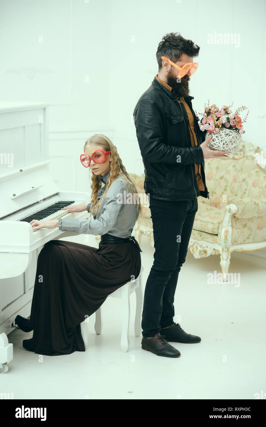 Conceptual fashion photo. Girl in dark maxi skirt playing piano while  stylish bearded man in leather jacket stands holding vase with flowers.  Models Stock Photo - Alamy