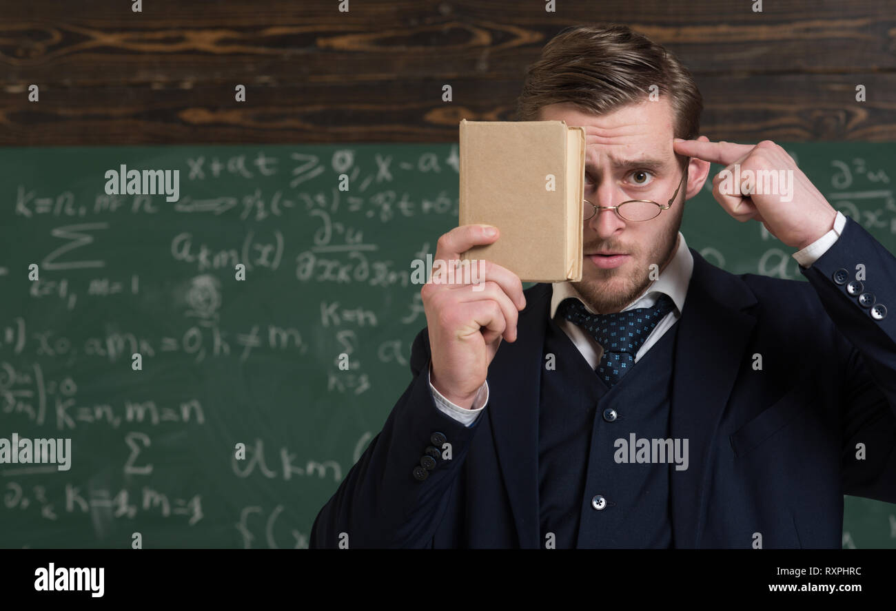 Closeup portrait of student holding book in front of his face and pressing finger over forehead. Thoughtful intelligent man in classroom Stock Photo