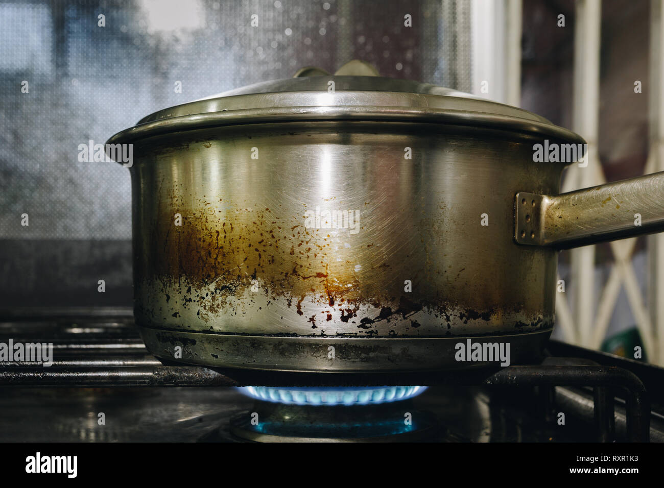 Old stainless steel handy pot on stove. Gas hob cooker flame alight, close-up Stock Photo
