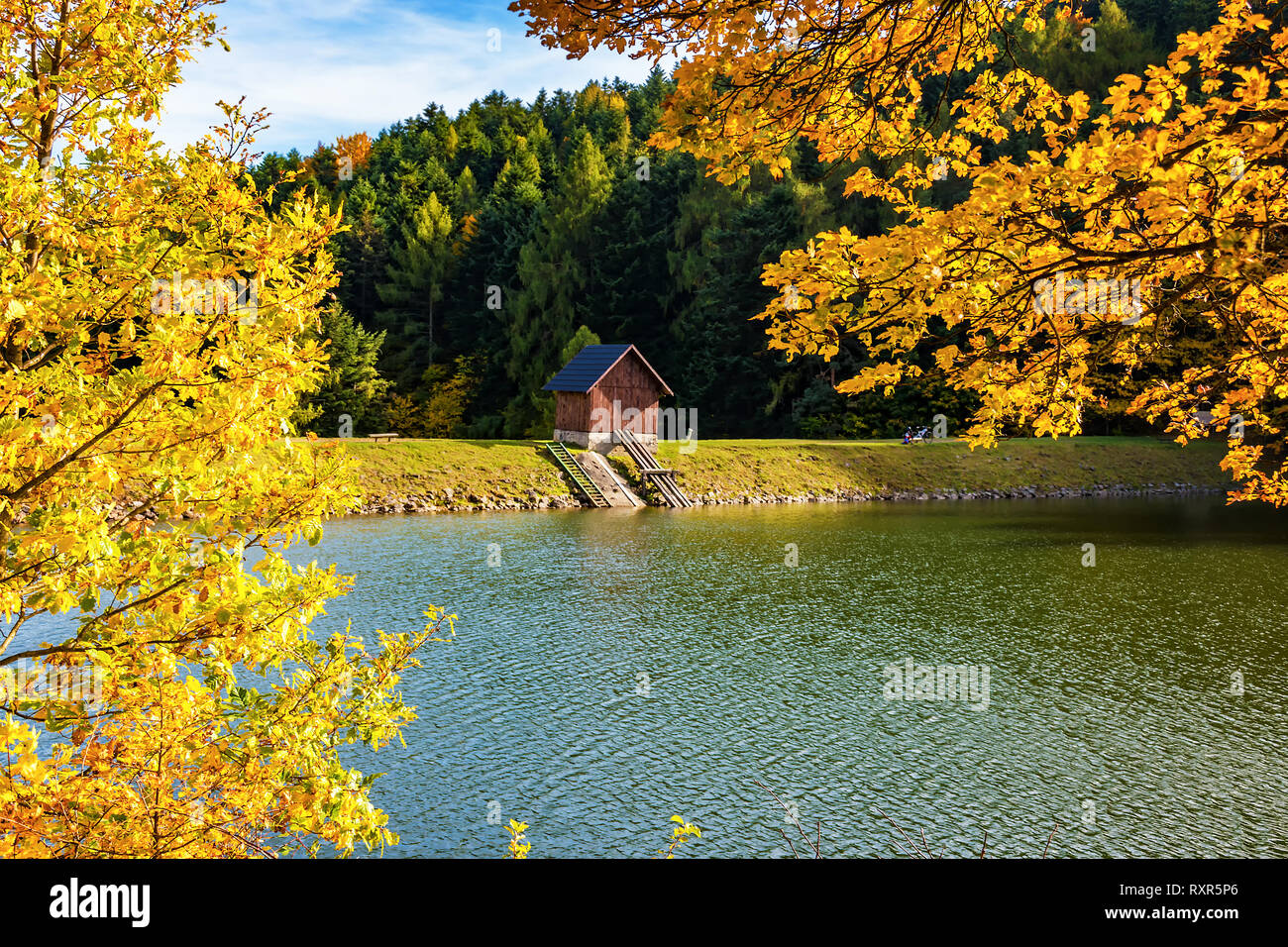 Beautiful view of small wooden house on bank of lake near forest during autumn Stock Photo