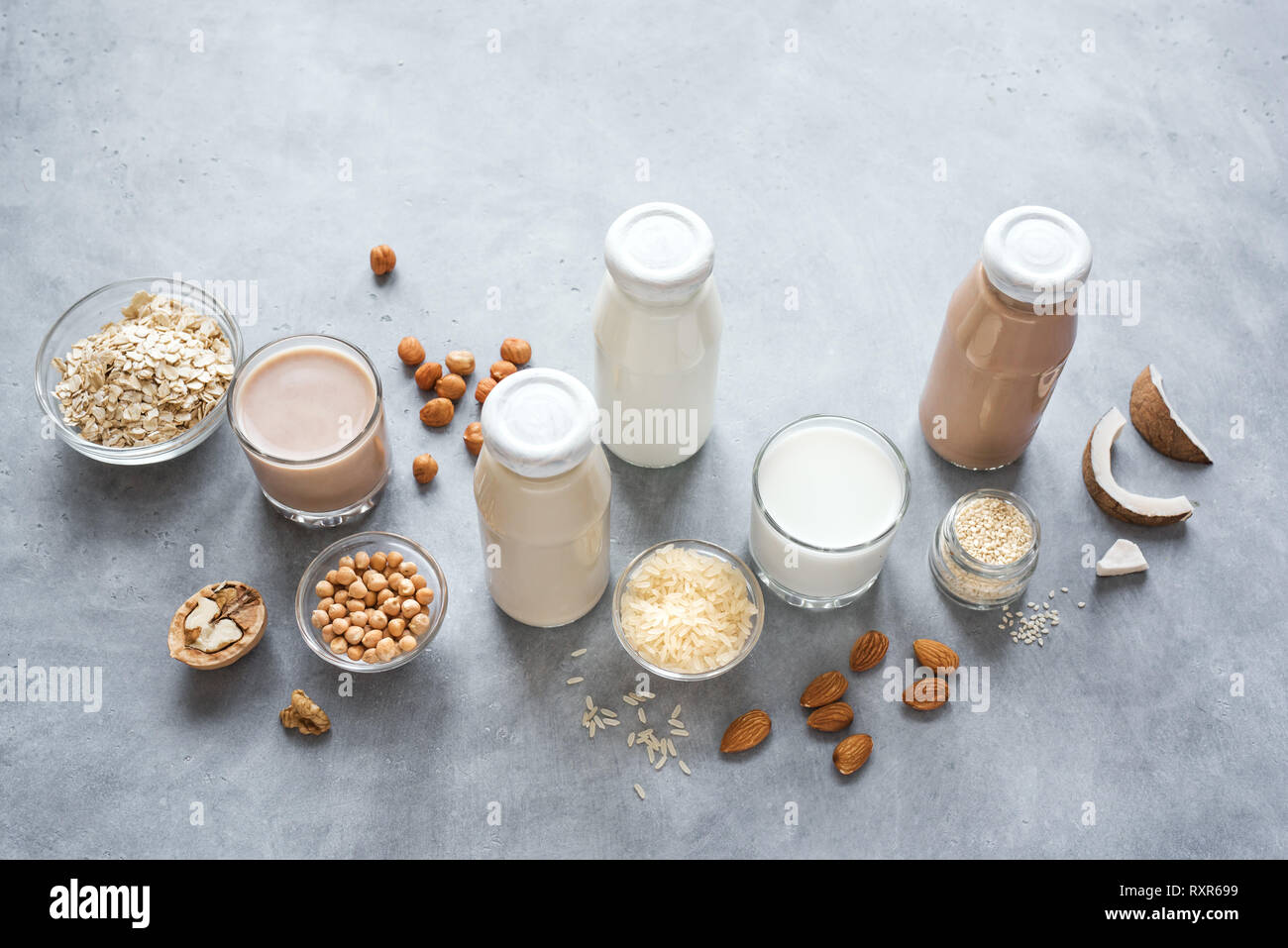 Various vegan plant based milk and ingredients on grey, copy space. Dairy free milk substitute drink, healthy eating. Stock Photo
