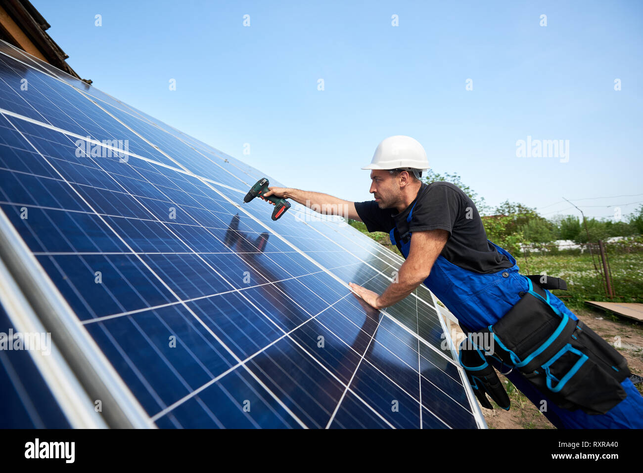 Profile of technician installing solar panel using electrical screwdriver on blue sky copy space