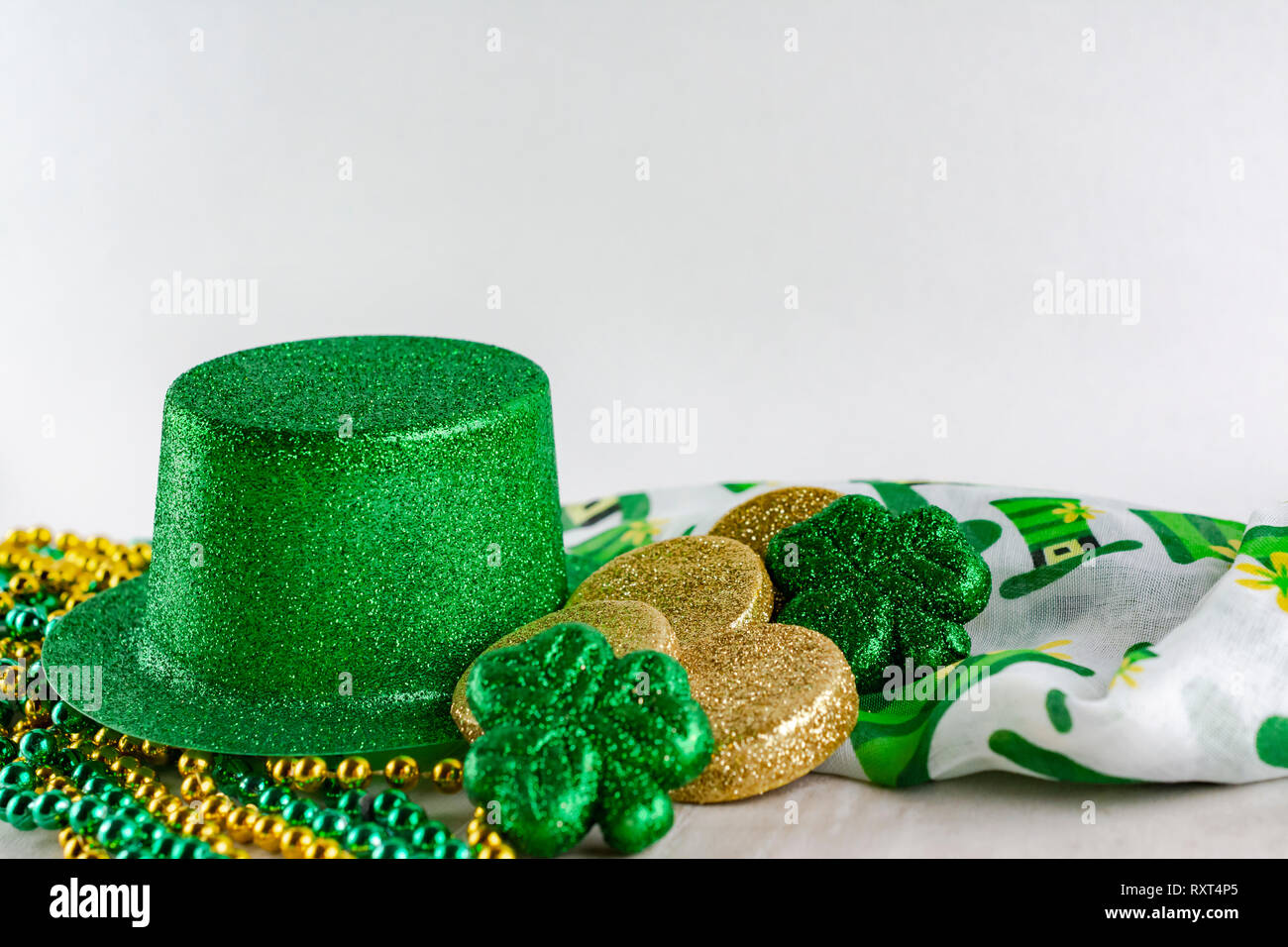 Saint Patrick's Day green top hat with gold coins, green shamrocks, green and gold beads, and colorful scarf.  White background with copy space above. Stock Photo