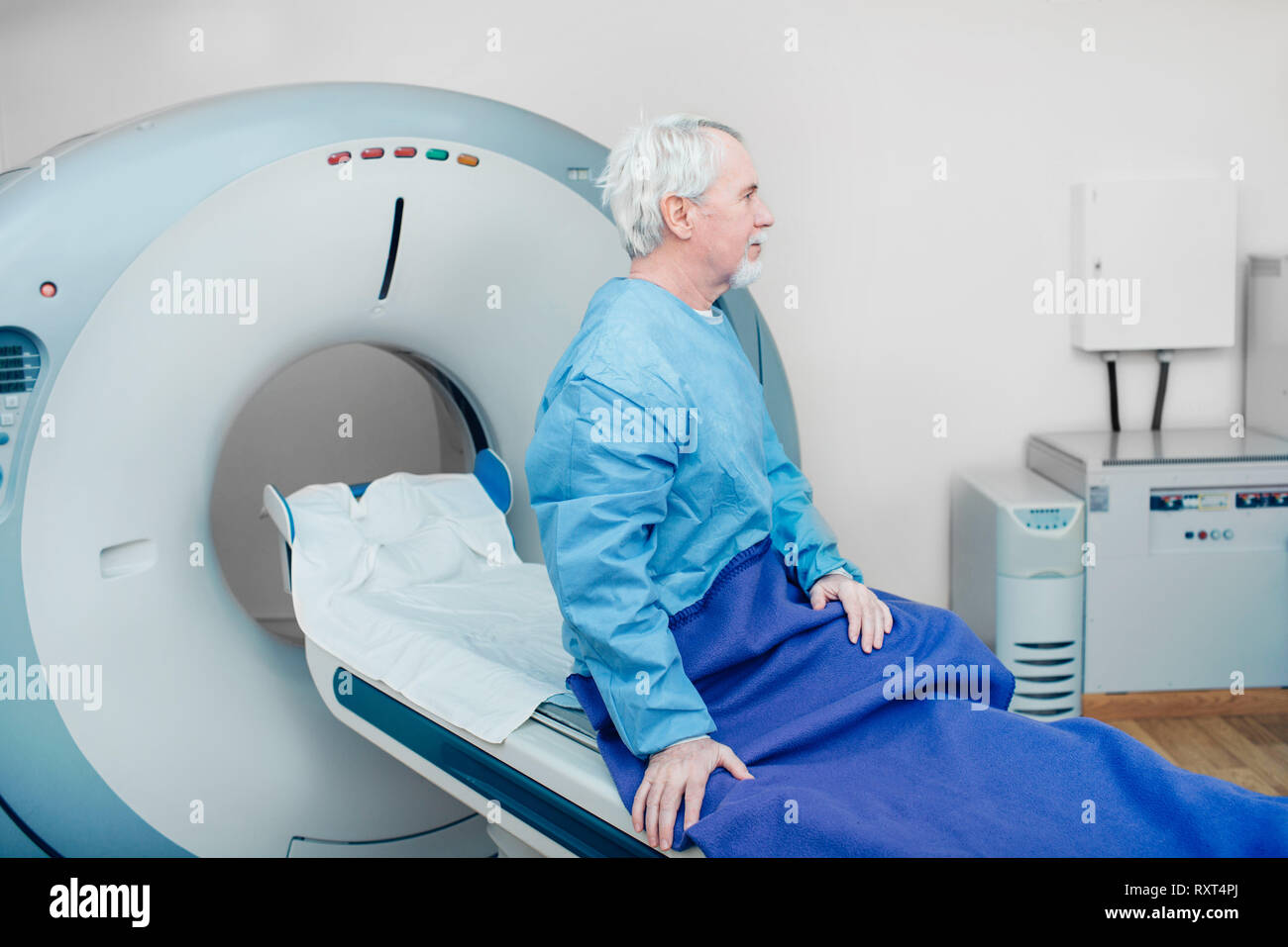 Pensive senior man sitting on scanner table. waiting for CT scan Stock Photo