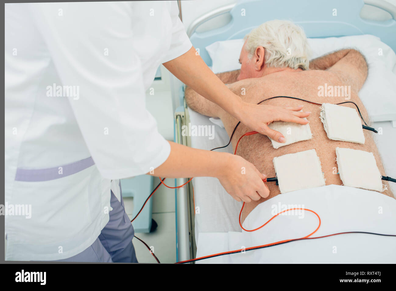 Physiotherapeutic treatment. Senior patient having ultrasound and electrotherapy treatment on his back Stock Photo
