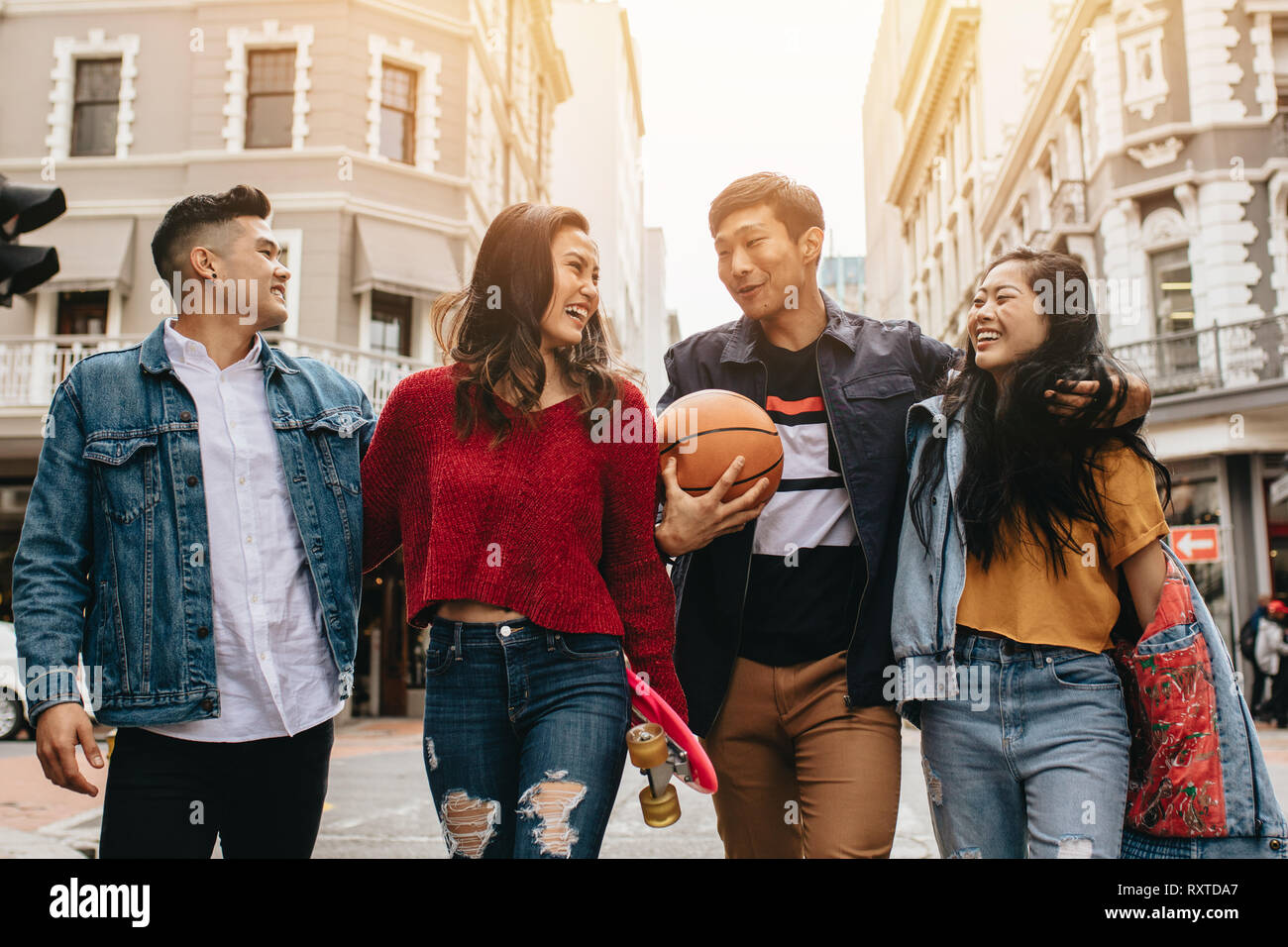 Group of men and women walking outdoors with skateboard and basketball. Two couples walking on city street. Stock Photo