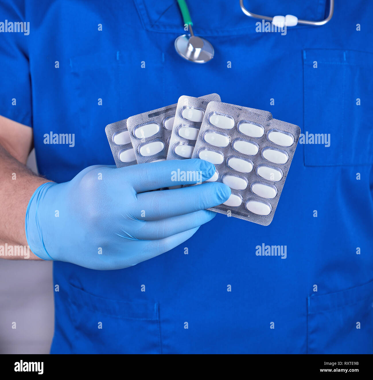 doctor in blue uniform and sterile gloves holding white pills in pack Stock Photo
