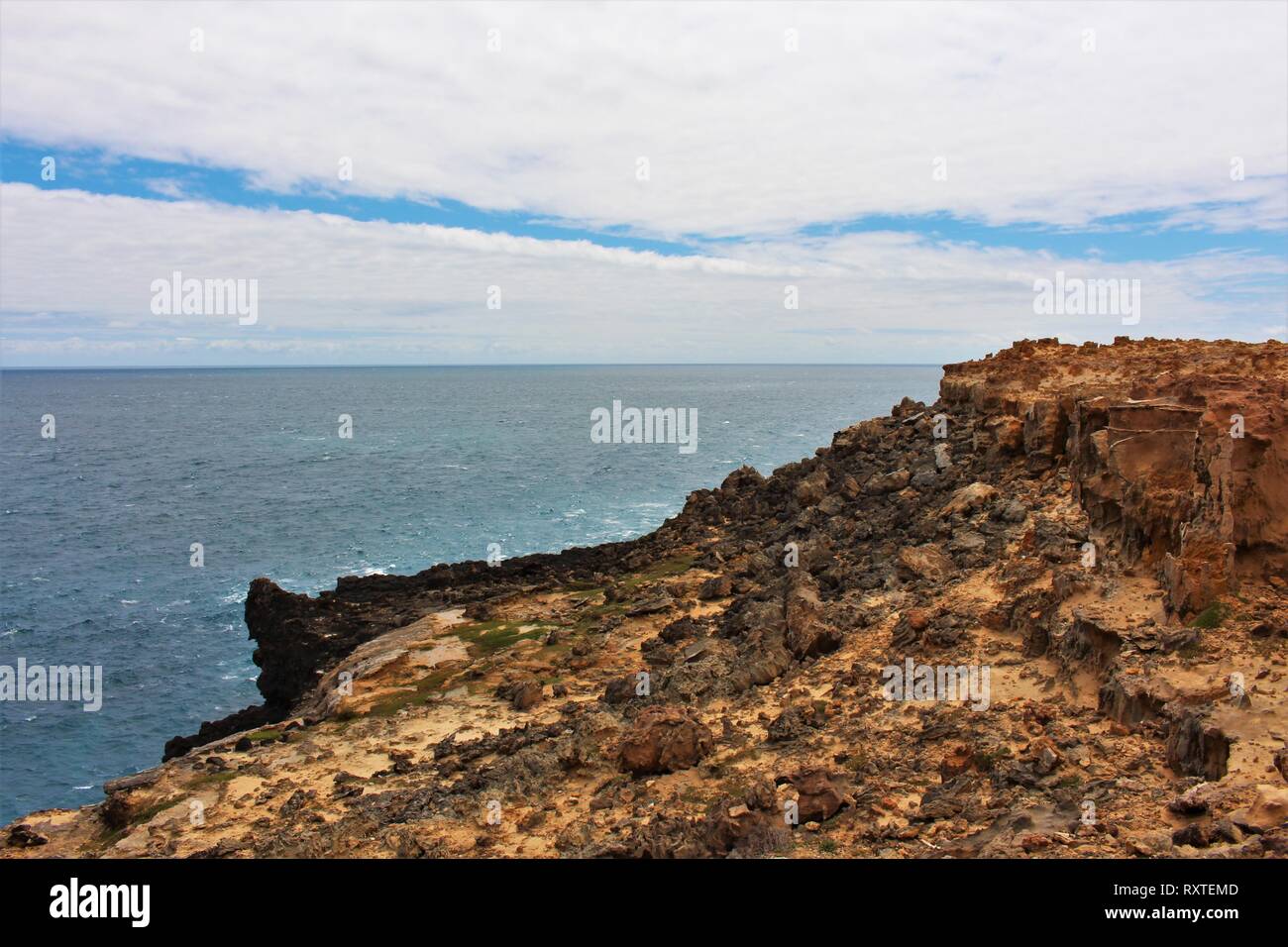 Striking sandy rock formations with black rocks and the ocean in the background at the petrified forest, on the south coast of Australia Stock Photo