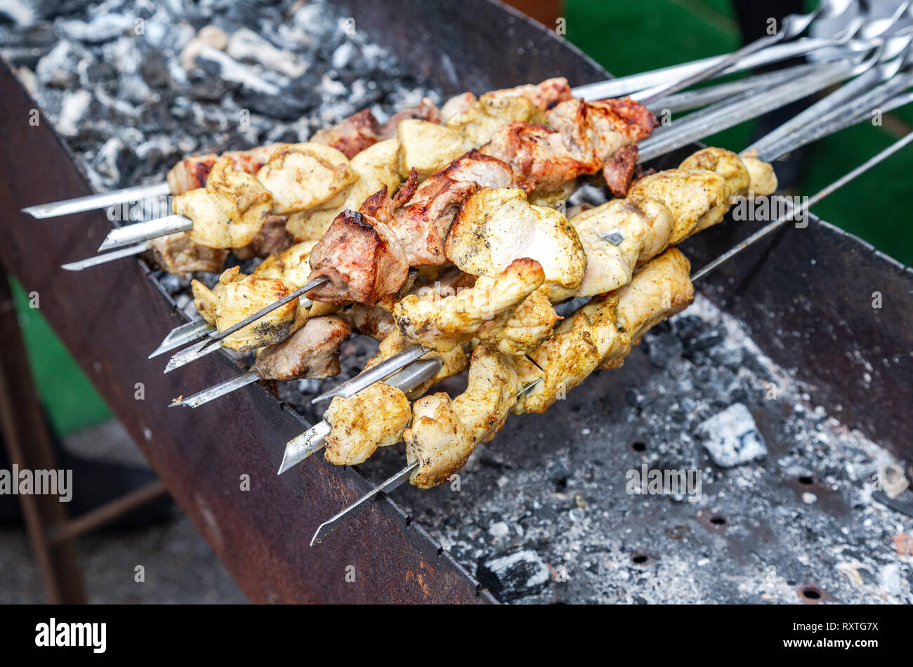 Grilled appetizing kebab cooking on metal skewers. Shashlik made of cubes of meat during of cooking on the mangal over hot charcoals outdoors, street  Stock Photo