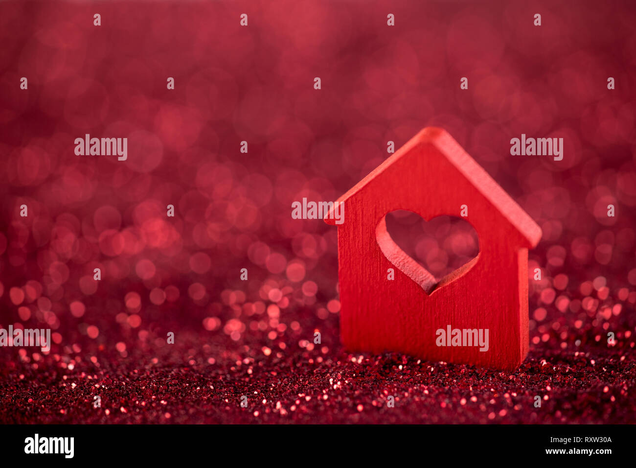 Small house with heart shape on red glitter background Stock Photo