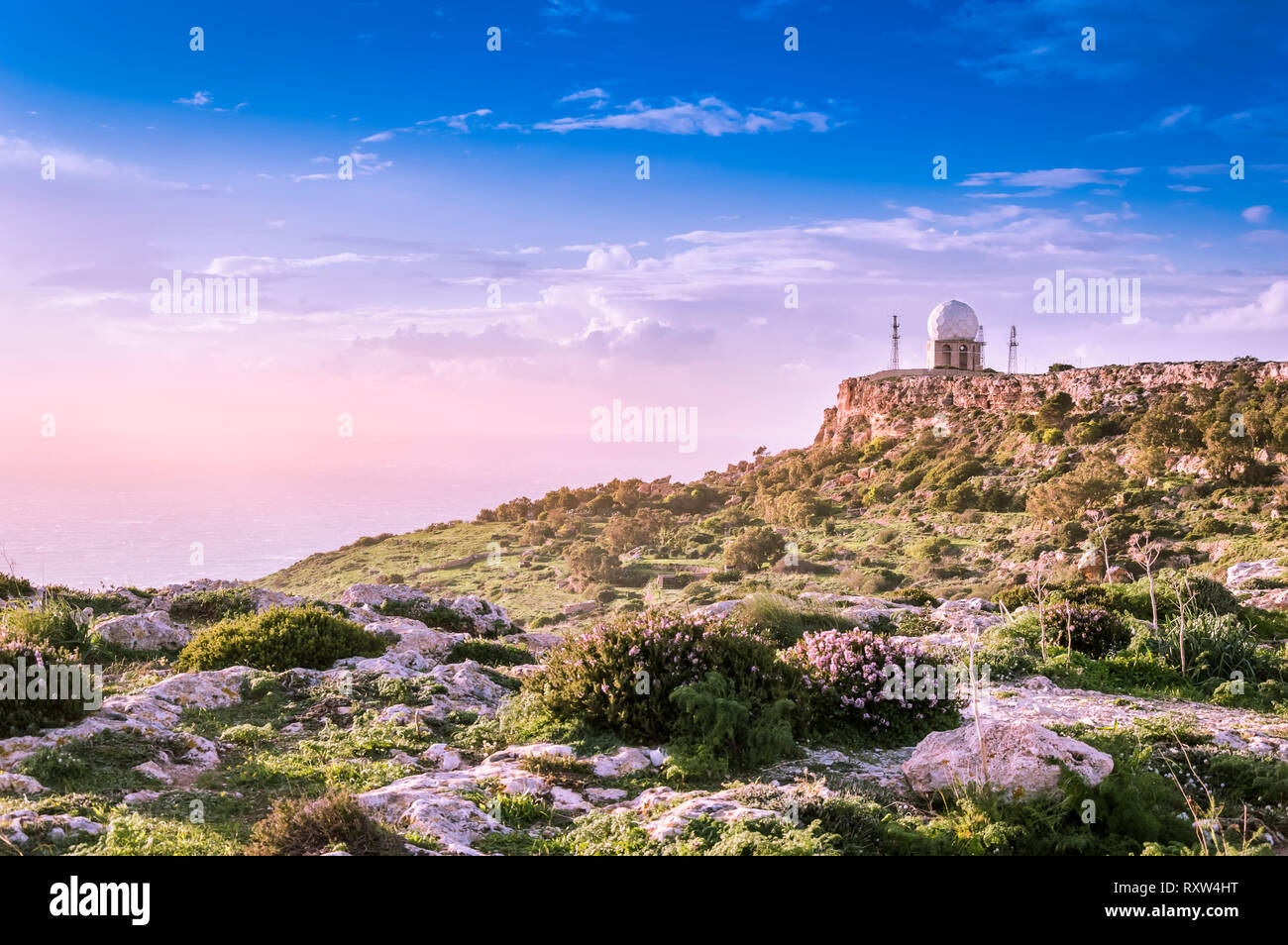 Dingli Cliffs, Malta: Panoramic road with a view over Dingli Cliffs and Aviation radar with lila flowers in forground. Romantic purple toning Stock Photo