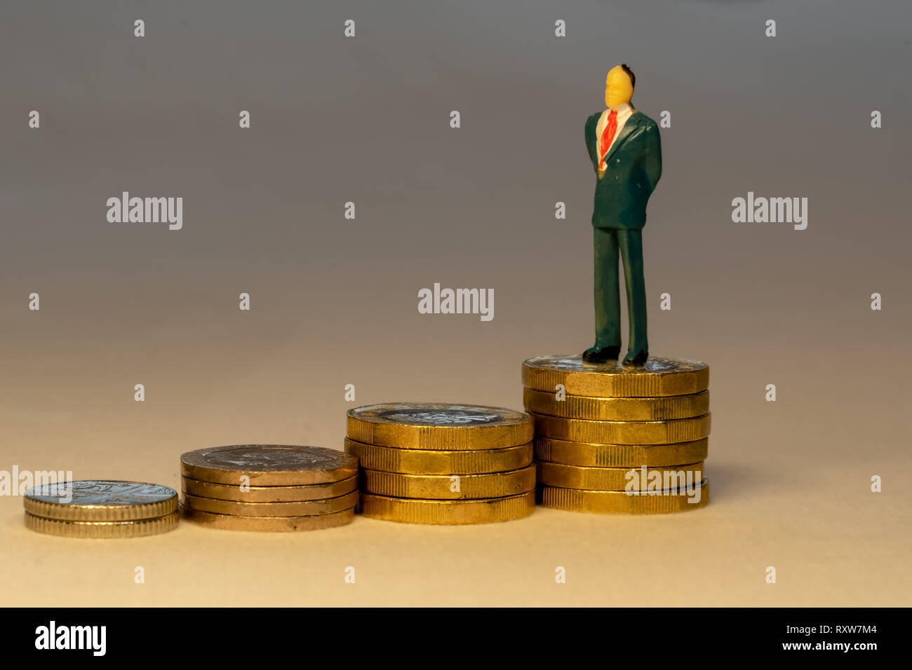 Rich successful businessman standing on top of increasing piles of gold coins. Business career concept. Stock Photo