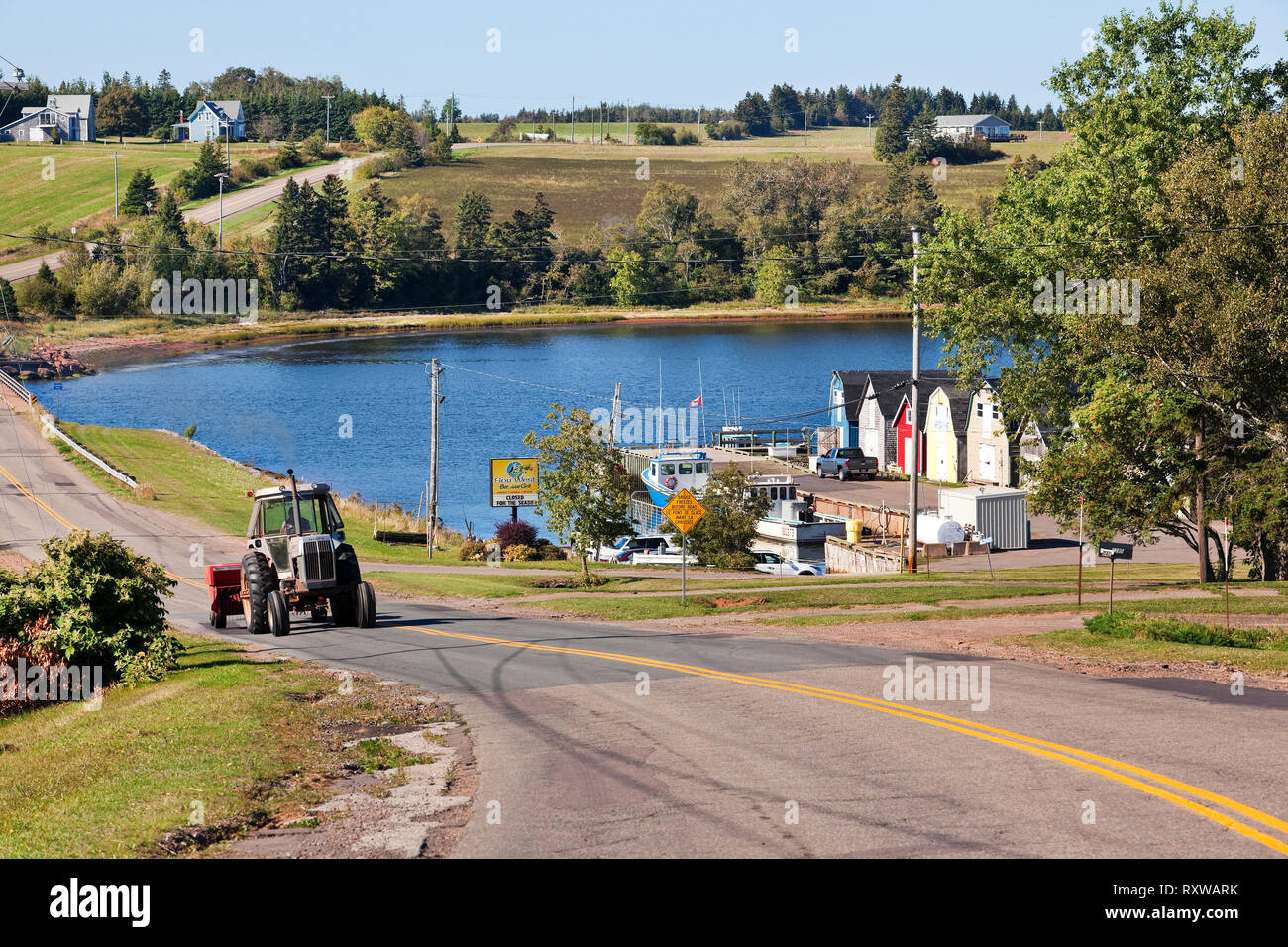 Farmland on rolling hills, New London Bay, wharf, and tractor on the move in New London, Prince Edward Island, Canada Stock Photo